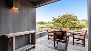 Um deck de madeira com um banco e cadeiras, com vista para um jardim ajardinado.