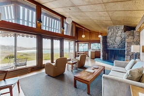 A spacious living area with large windows, a stone fireplace, and a view of the ocean. - Oceanfront home with fireplace near Black Point Beach, dogs welcome (Sea Ranch)