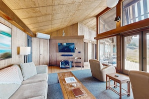 A spacious living area with a wooden ceiling, a large TV, and a view through the glass doors. - Oceanfront home with fireplace near Black Point Beach, dogs welcome (Sea Ranch)