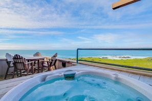 Ein Whirlpool auf einer Terrasse mit Stühlen und einem Tisch, mit Blick auf einen Strand und den Ozean.