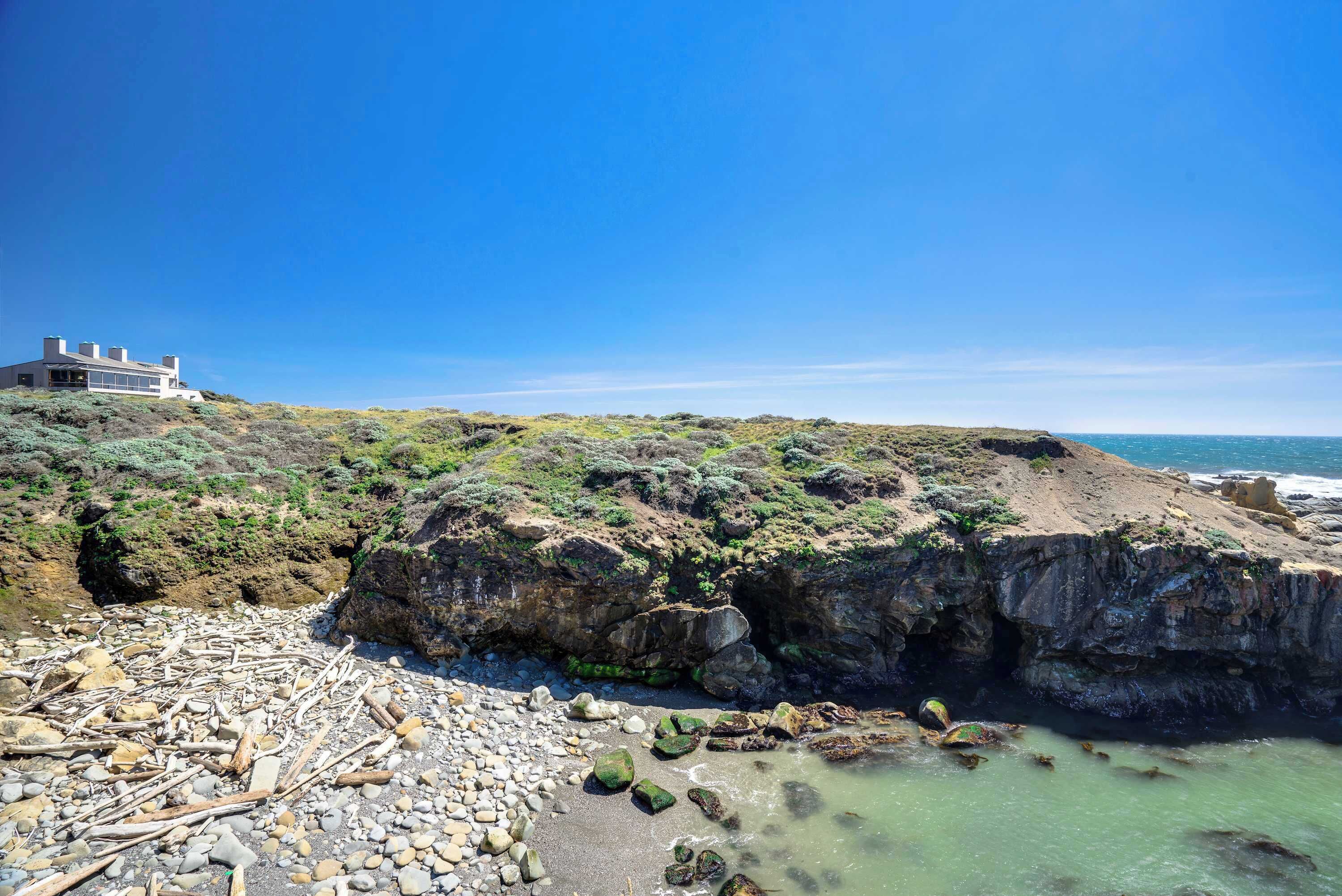 Eine Küstenlandschaft mit einem modernen Gebäude auf einem Hügel, felsiger Küstenlinie und blauem Himmel.