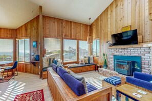 A wooden interior with a fireplace, seating area, and large windows. - Ocean-view meadow home with deck & grill near Black Point, dogs welcome (Sea Ranch)
