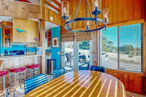 A dining area with a large table and bar stools, a kitchen with wooden cabinets, and a view through the window. - Ocean-view meadow home with deck & grill near Black Point, dogs welcome (Sea Ranch)