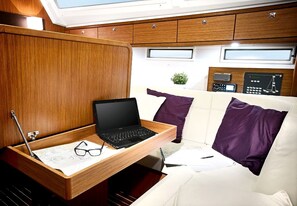 A compact living space with a laptop on a wooden tray, a white couch with purple pillows, and a small plant. - Sun-Kissed Sailing Adventure in Islas Esporadas (Skiathos)