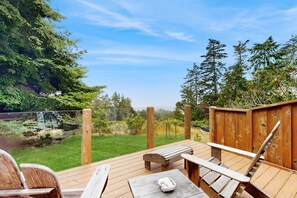 A wooden deck with a bench and table, surrounded by a wooden fence and trees. - Ocean-view home with fireplace & courtyard near Pebble Beach (Sea Ranch)