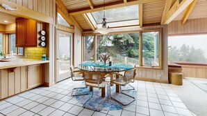 Un intérieur en bois avec une table à manger en verre, des chaises et une vue dégagée grâce à de grandes fenêtres.