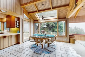 A wooden interior with a glass dining table, chairs, and a view through large windows. - Ocean-view home with fireplace & courtyard near Pebble Beach (Sea Ranch)