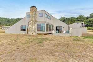 A modern house with a stone chimney, large windows, and a grassy yard. - Sea Ranch home with private hot tub near beach & playground (Sea Ranch)