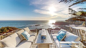 Eine Terrasse mit Sitzgelegenheiten und Geländer, mit Blick auf das Meer.