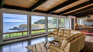Ein großzügiger Wohnbereich mit einem großen Fenster zum Meer, einer Ledersofa und einer Küche im Hintergrund.