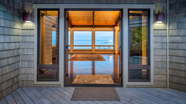 Ein moderner Gebäudeeingang mit Glastüren, Holzboden und Blick aufs Meer.