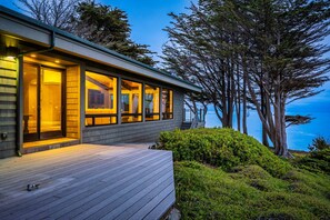 Een modern huis met een houten terras, grote ramen en uitzicht op zee.