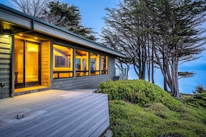 A modern building with large windows, a wooden deck, and a view of the ocean. - Blufftop home with hot tub & forever oceanfront views & private cottage (Gualala)