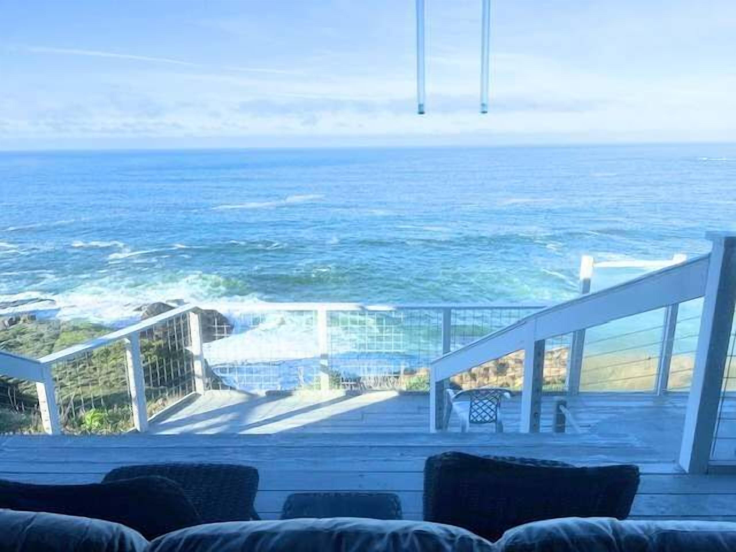 A deck with a view of the ocean, a railing, and a staircase leading to a higher level.