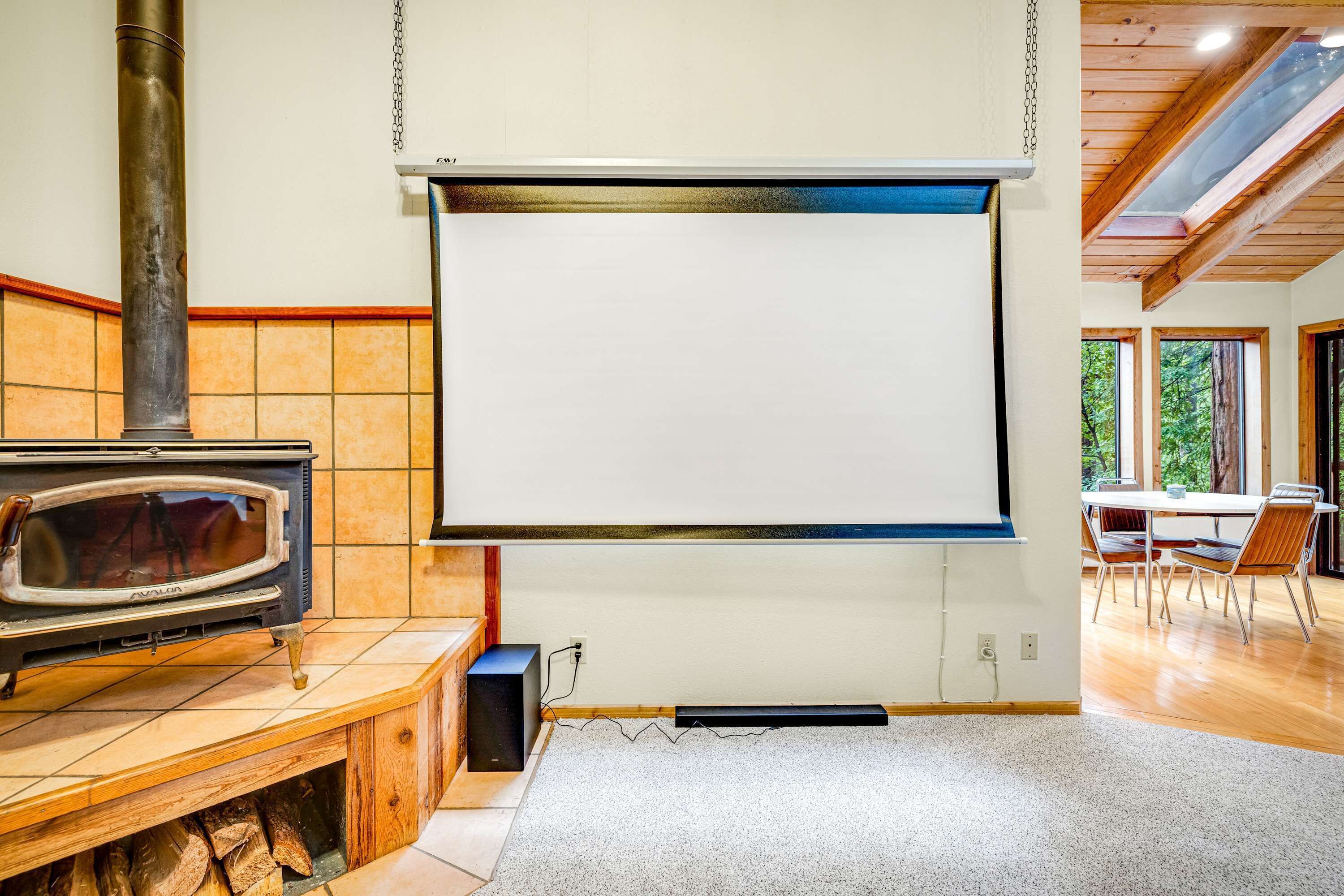 A room with a fireplace, a projector screen, and a dining area with chairs.