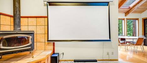 A room with a fireplace, a projector screen, and a dining area with chairs.