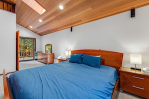 Ein Schlafzimmer mit einem großen Bett, einem Holz-Kopfteil, einem Nachttisch mit Lampe, einer Kommode und einer Glastür zu einem Balkon.