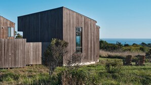 Een modern houten gebouw met een groot raam, gelegen in een grasrijk gebied met uitzicht op de oceaan.