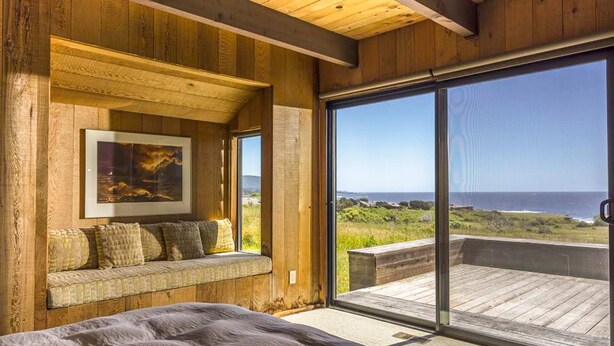 A bedroom with a large window, a wooden bench, and a framed picture. - Rare Ocean Views & Sea Ranch Magic on the Mendocino Coast (Sea Ranch)