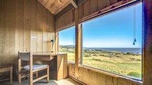 A wooden room with a desk and chair, large windows with a view of a grassy landscape. - Rare Ocean Views & Sea Ranch Magic on the Mendocino Coast (Sea Ranch)