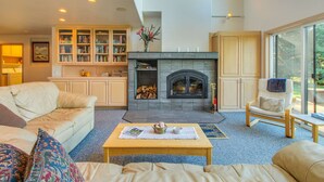 Ein Wohnzimmer mit Kamin, Bücherregalen, einer Couch, einem Sessel und einem Couchtisch.