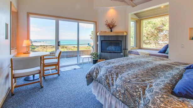 Ein Schlafzimmer mit Bett, Schreibtisch mit Stuhl, Kamin und Meerblick.