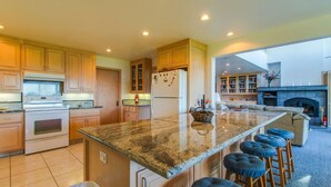 Eine geräumige Küche mit Granit-Arbeitsplatten, Holzschränken, einer großen Kücheninsel mit Barhocker und einem Kamin im Wohnbereich.