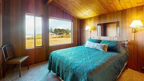 A bedroom with a large bed, wooden walls, a window with a view, and a chair. - Sea Ranch 2BR getaway with ocean views, wood stove & private deck (Sea Ranch)