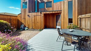 A modern wooden house with a patio, outdoor seating, and a chimney. - Sea Ranch 2BR getaway with ocean views, wood stove & private deck (Sea Ranch)