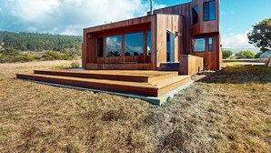 A modern wooden house with large windows, a chimney, and a wooden deck. - Sea Ranch 2BR getaway with ocean views, wood stove & private deck (Sea Ranch)