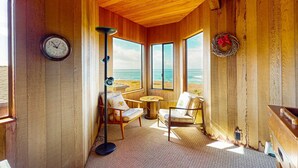 A wooden interior with a clock, two chairs, a floor lamp, and a view of the ocean. - Sea Ranch 2BR getaway with ocean views, wood stove & private deck (Sea Ranch)