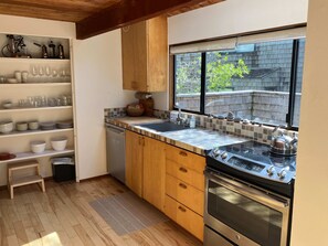 A modern kitchen with wooden cabinets, a stainless steel stove, and a window with a view of the outside. - Sea Ranch 2BR timber-frame home with hot tub near Stengel Beach (Sea Ranch)