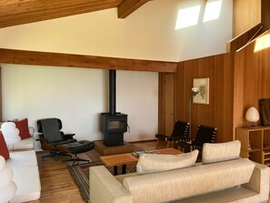 A cozy living room with a fireplace, wooden beams, a sofa, chairs, and a small table. - Sea Ranch 2BR timber-frame home with hot tub near Stengel Beach (Sea Ranch)