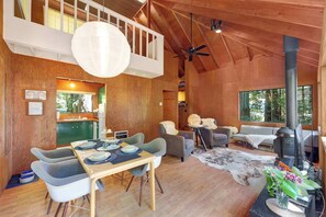Un interior de madera con comedor, sofás, chimenea y vistas amplias a través de grandes ventanales.