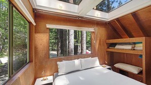 Een slaapkamer met dakraam, een bed, een nachtkastje en een houten plank.