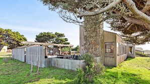 A modern house with a stone wall, wooden deck, and outdoor seating area. - Sea Ranch 3BR distant ocean-view home with hot tub — dogs welcome (Sea Ranch)