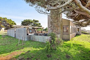 A modern house with a stone wall, wooden deck, and outdoor seating area. - Distant ocean-view home with hot tub near Walk On Beach, dogs welcome (Sea Ranch)