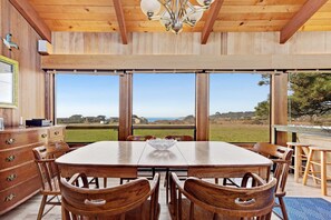 A wooden dining table with chairs, a chandelier, and large windows with a view of the landscape. - Distant ocean-view home with hot tub near Walk On Beach, dogs welcome (Sea Ranch)