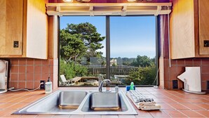 A kitchen with a large window, two sinks, and a view of greenery outside. - Sea Ranch 3BR distant ocean-view home with hot tub — dogs welcome (Sea Ranch)