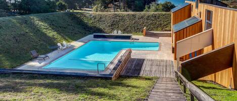 A modern pool area with a wooden deck and a view of the ocean.
