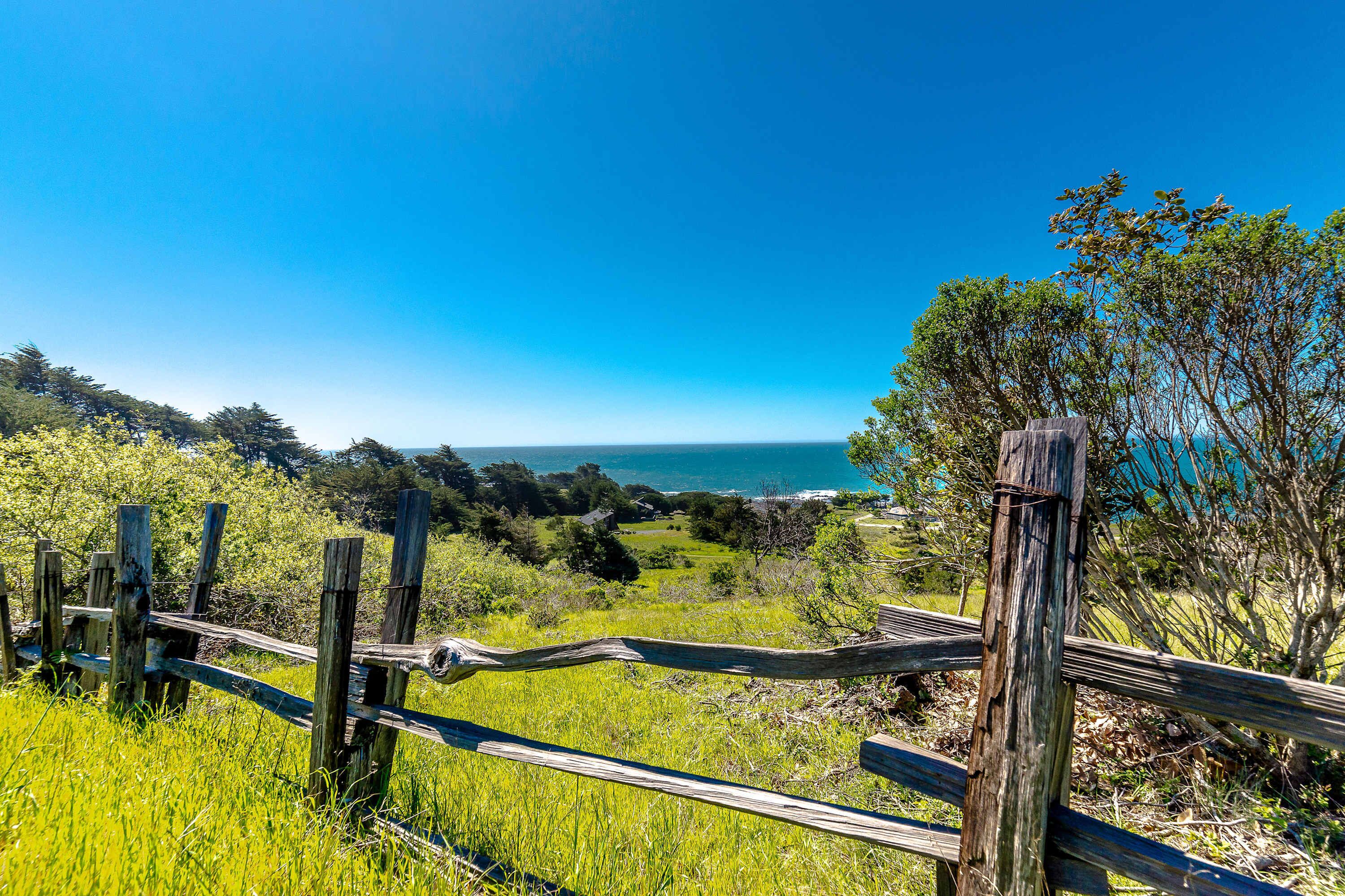 A wooden fence with a view of the ocean and greenery.