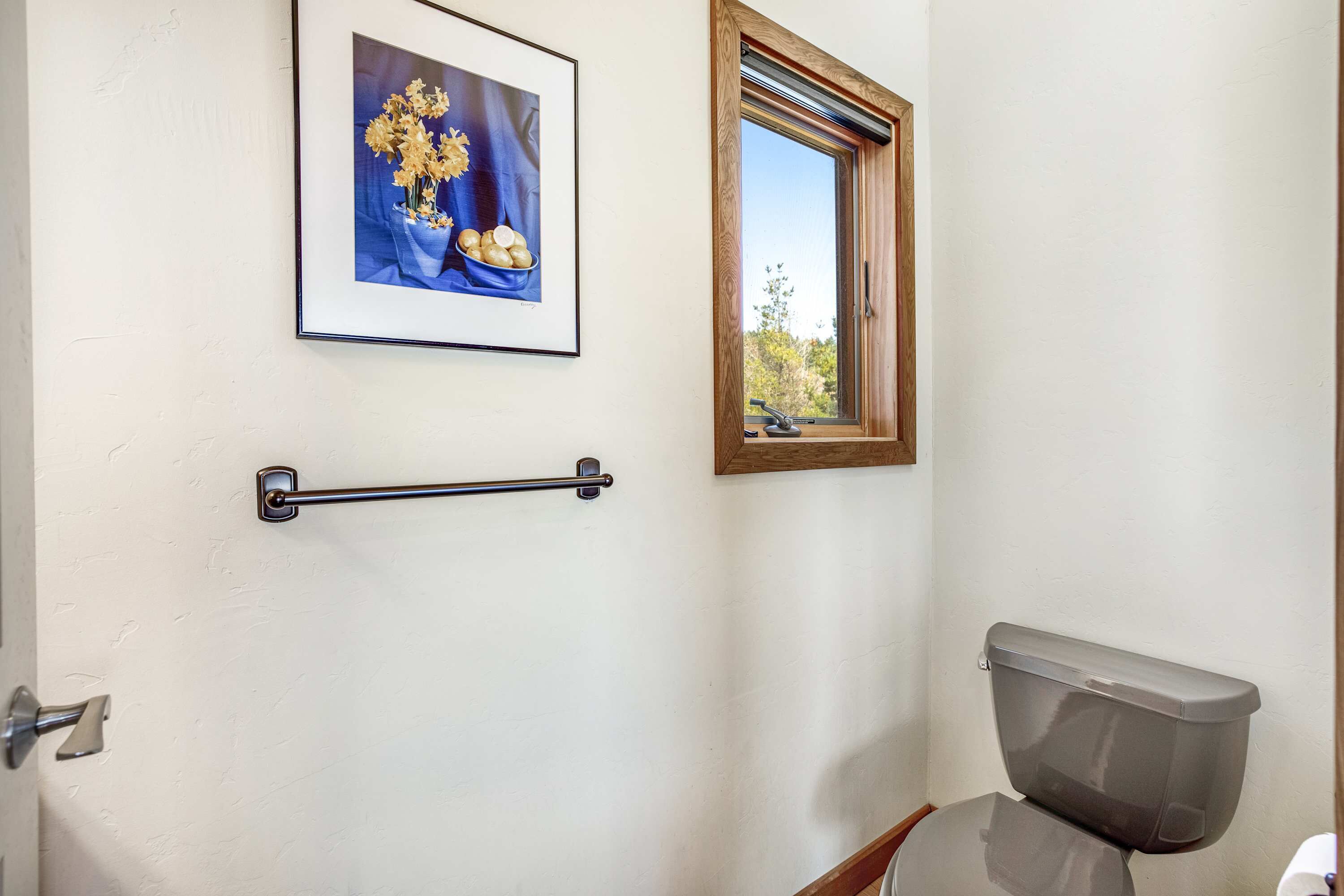 A bathroom with a toilet, a towel rack, a window, and a framed picture on the wall.