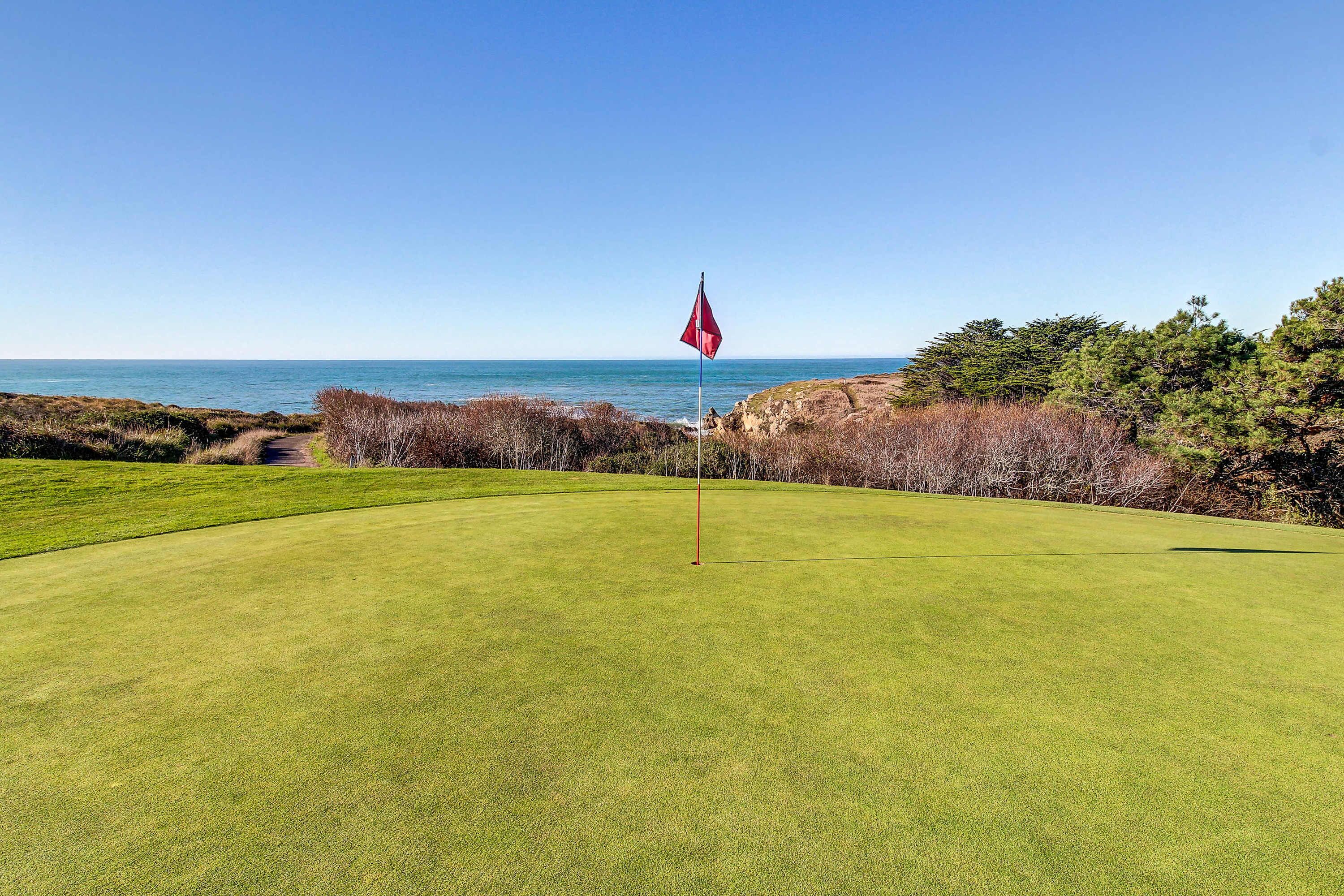 Campo de golf con una bandera, vista al océano y cielo despejado.
