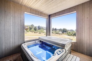 A wooden room with a hot tub, large windows, and a view of a landscape. - Ocean-view home with private hot tub near Pebble Beach (Sea Ranch)
