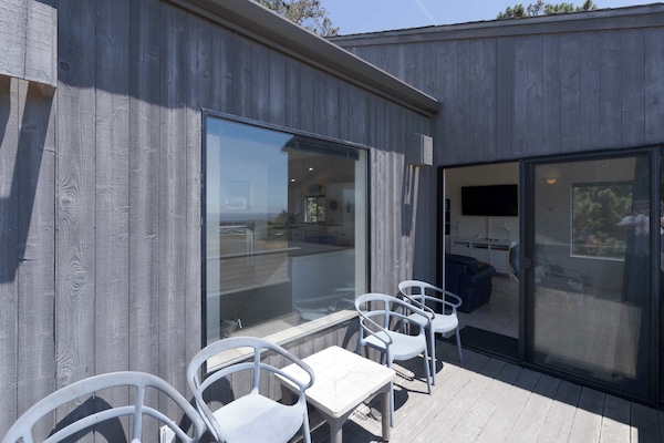 Lounge on the wraparound deck where sliding doors open straight to the living room, blurring the line between indoors and ocean air.
