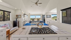 Una cocina moderna con estufa a gas, ventilador de techo y grandes ventanales con vistas al exterior.