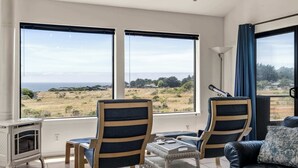 Una habitación con dos sillas frente a un ventanal grande, un sofá, una mesita y una lámpara.