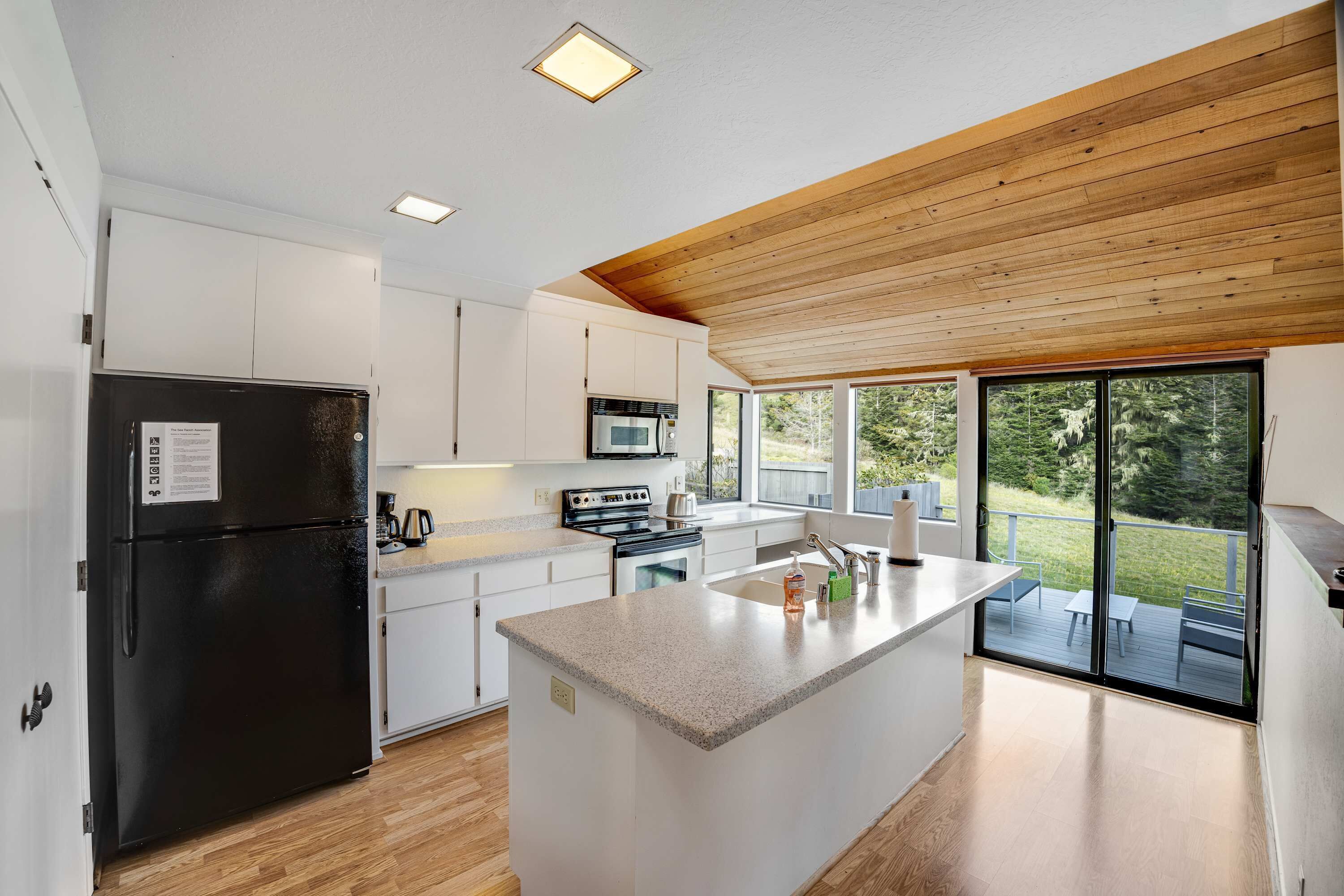 A modern kitchen with white cabinets, a black refrigerator, and a wooden ceiling.