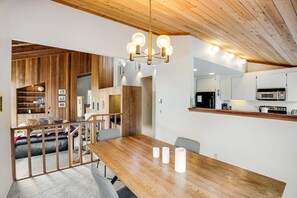 A modern interior with a wooden dining table, a chandelier, and a kitchen area. - Sea Ranch meadow home with fireplace & panoramic ocean views (Sea Ranch)