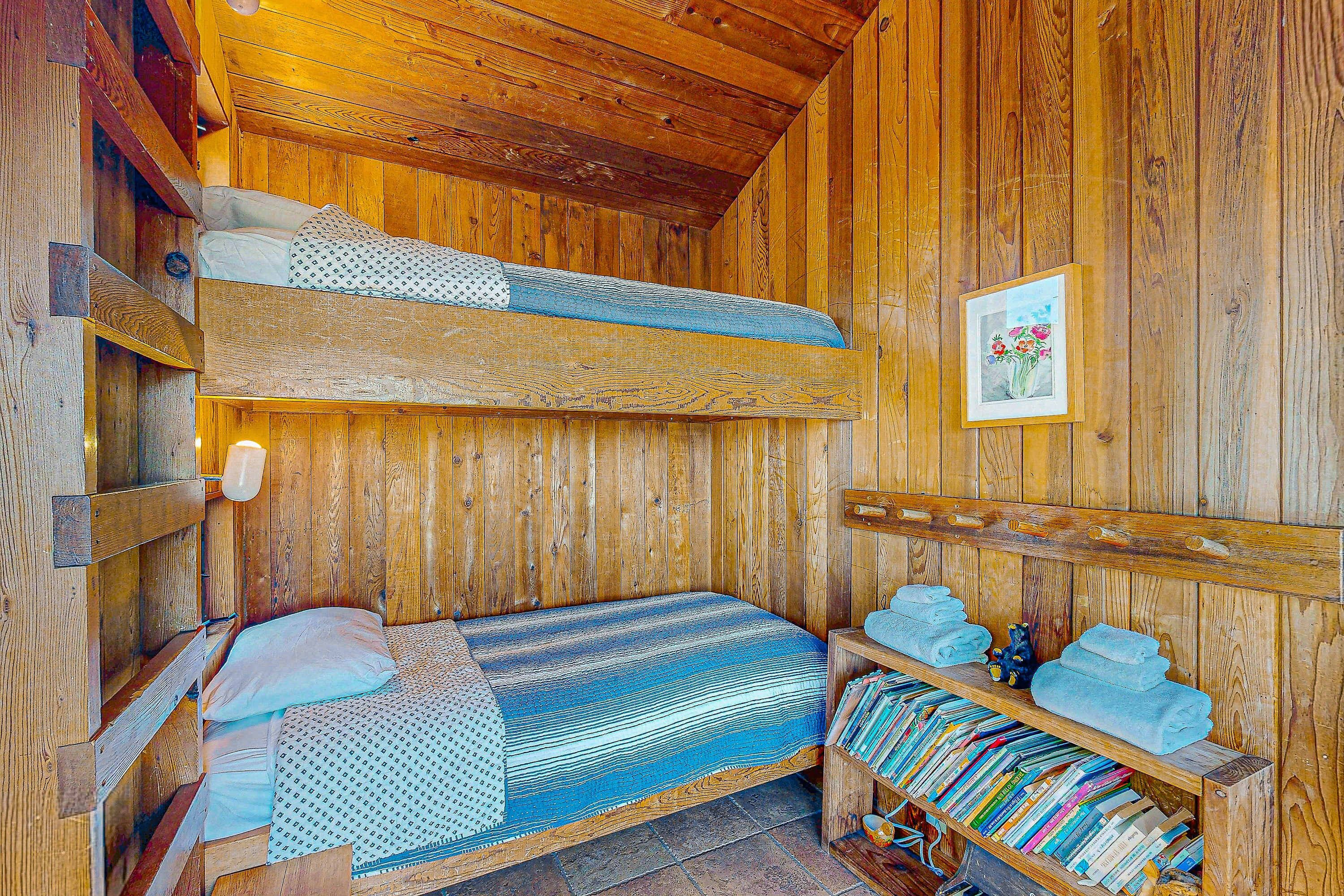 A wooden cabin with bunk beds, a shelf with towels, and a framed picture on the wall.